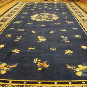 Deep blue area rug featuring gold bird and floral designs, laid on bright yellow wood flooring.