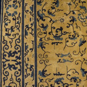 Gold rug with dark blue scrolling vines and floral border detail on wood plank flooring.