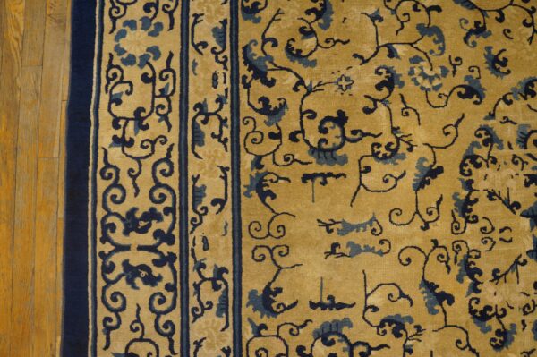 Gold rug with dark blue scrolling vines and floral border detail on wood plank flooring.