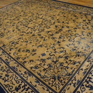 Gold rug with complex navy and blue floral motifs, thick borders, resting on wood flooring.
