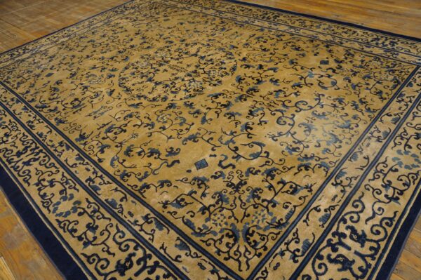 Gold rug with complex navy and blue floral motifs, thick borders, resting on wood flooring.