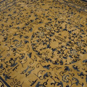A gold rug with dark blue floral scrollwork and borders rests on light wood floors.