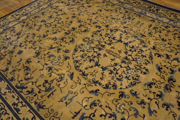 A gold rug with dark blue floral scrollwork and borders rests on light wood floors.
