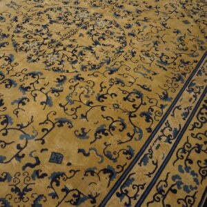 Gold rug with dark and light blue scrolling vine patterns and bordered edges on wood flooring.