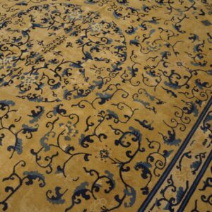 Detailed view of a gold rug with an intricate blue floral pattern and a dark striped border.