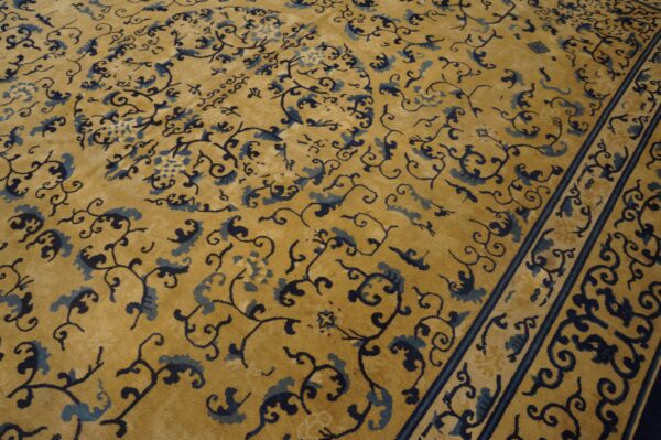 Detailed view of a gold rug with an intricate blue floral pattern and a dark striped border.