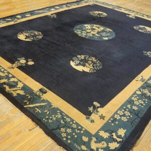 Dark blue rug with tan and teal floral medallions and intricate borders on light wood flooring.