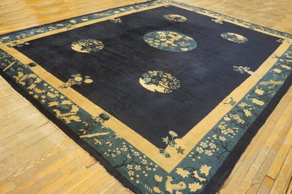 Dark blue rug with tan and teal floral medallions and intricate borders on light wood flooring.