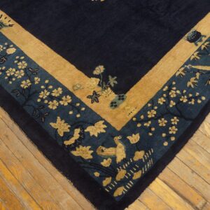 Corner of a navy rug featuring gold and teal floral and bird borders resting on light wooden planks.