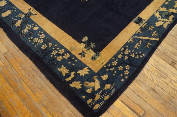 Corner of a navy rug featuring gold and teal floral and bird borders resting on light wooden planks.