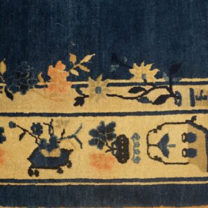 Dark blue rug border on distressed wood, showing beige panels with navy and peach floral motifs.