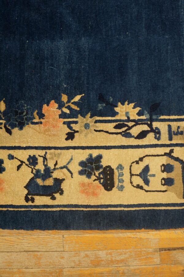 Dark blue rug border on distressed wood, showing beige panels with navy and peach floral motifs.