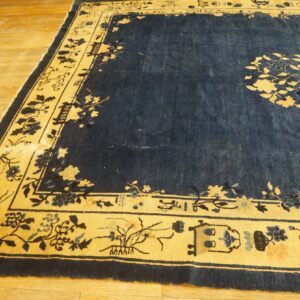 Navy blue rug with a golden border and botanical patterns lies on light hardwood flooring.