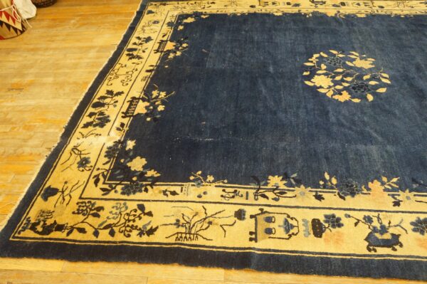 Navy blue rug with a golden border and botanical patterns lies on light hardwood flooring.