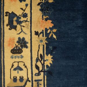 Low-pile rug with navy blue field and tan border featuring stylized indigo and coral floral motifs on wood flooring.