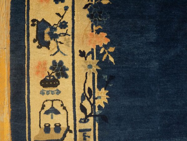 Low-pile rug with navy blue field and tan border featuring stylized indigo and coral floral motifs on wood flooring.