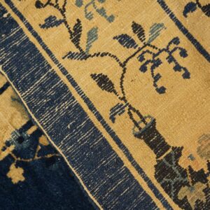 Close-up of a rug with tan and blue floral patterns folded against a solid dark blue pile.