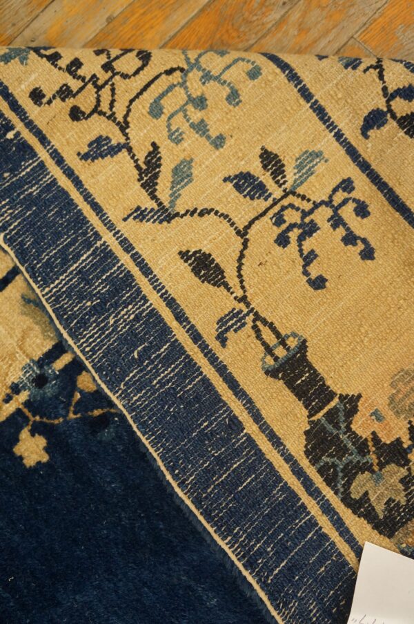 Close-up of a rug with tan and blue floral patterns folded against a solid dark blue pile.