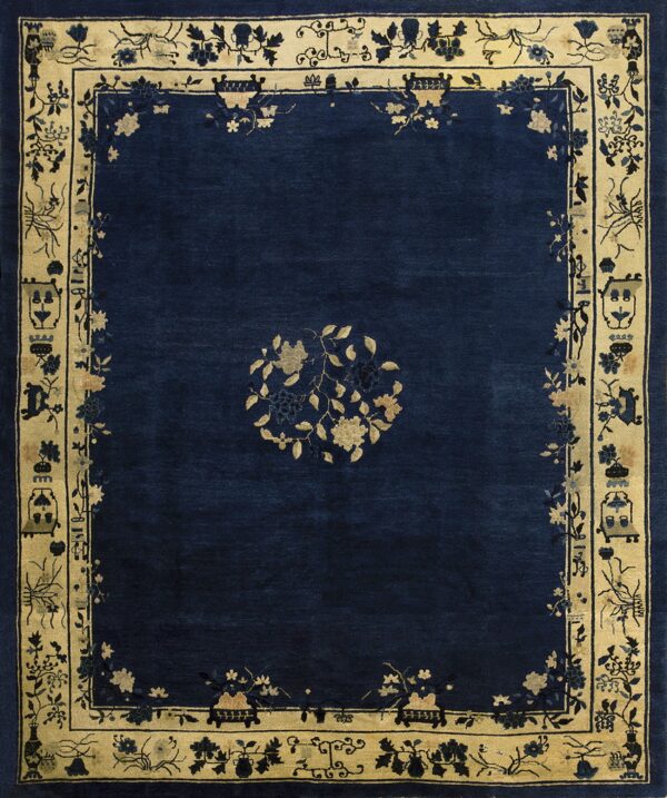 A navy blue rug features a central gold floral motif and an elaborate beige border with detailed patterns.