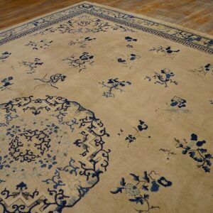 Angled view of a tan rug with dark blue stylized florals and geometric border on wood flooring.