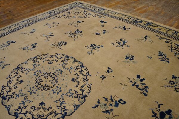 Angled view of a tan rug with dark blue stylized florals and geometric border on wood flooring.