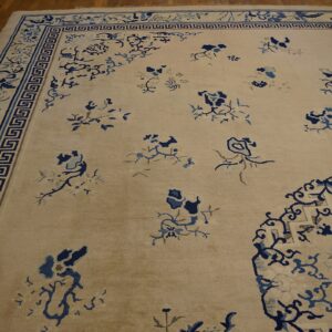 Light beige rug with scattered blue floral patterns and a wide ornamental key border on brown wood floors.