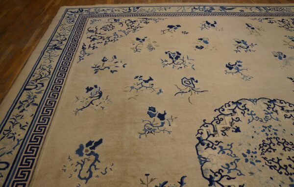 Light beige rug with scattered blue floral patterns and a wide ornamental key border on brown wood floors.