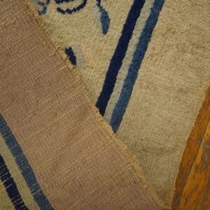 High-pile rug with tan and blue patterns is folded over its woven mauve backing on distressed wood planks.