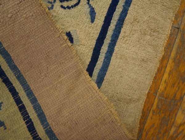 High-pile rug with tan and blue patterns is folded over its woven mauve backing on distressed wood planks.