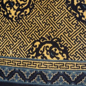 Geometric yellow and navy rug featuring maze and scroll patterns rests on honey-toned wood planks.