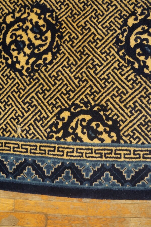 Geometric yellow and navy rug featuring maze and scroll patterns rests on honey-toned wood planks.