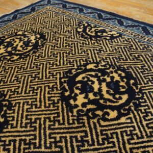Close-up of a dark blue and gold geometric lattice rug with floral medallions on light wood flooring.
