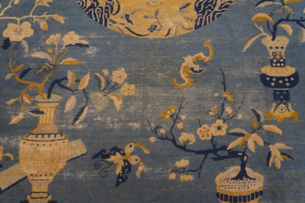 Close-up of a blue rug featuring yellow and cream floral branches emerging from stylized vases.