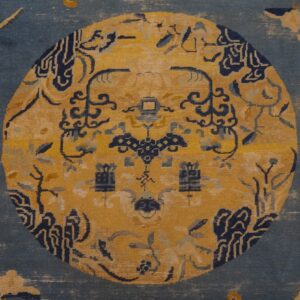 Muted blue rug detail featuring a large golden yellow medallion and stylized navy floral designs.