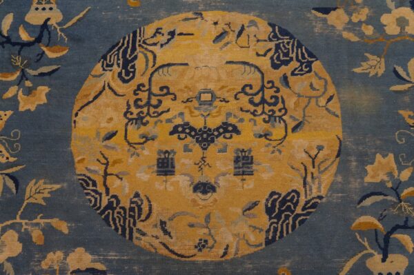 Muted blue rug detail featuring a large golden yellow medallion and stylized navy floral designs.
