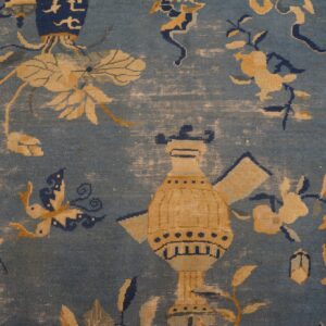 Distressed blue rug close-up features gold and navy motifs of a large vessel, flowers, and a butterfly.