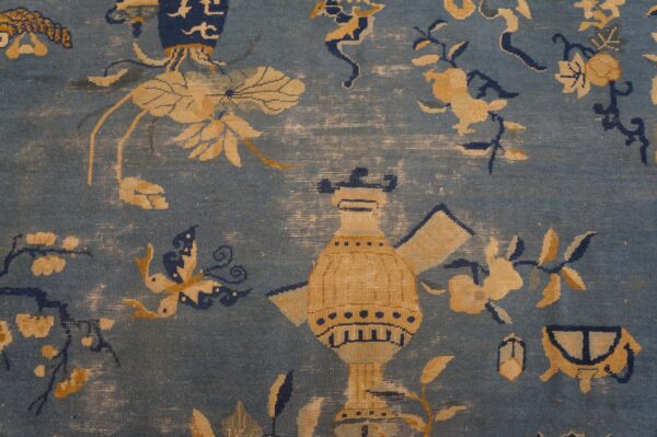 Distressed blue rug close-up features gold and navy motifs of a large vessel, flowers, and a butterfly.
