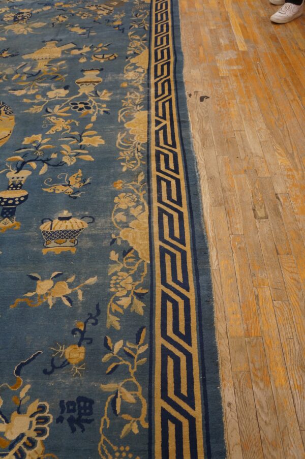 Blue rug with gold and navy botanical patterns and geometric border rests on worn wood flooring.
