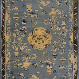 Muted blue rug patterned with tan and navy flowers, vases, and a large circular central medallion.