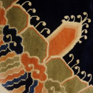 High-pile navy rug detailed with vibrant orange, green, and blue scrolling floral designs, showing fringe.
