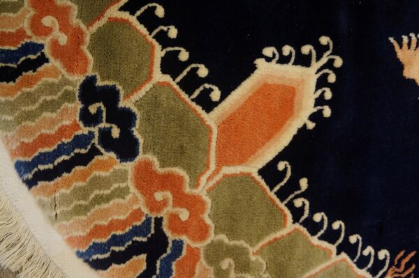 High-pile navy rug detailed with vibrant orange, green, and blue scrolling floral designs, showing fringe.