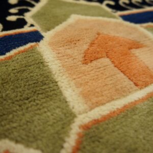 Close-up showing the rug's plush texture and geometric pattern in green, salmon, blue, and cream.