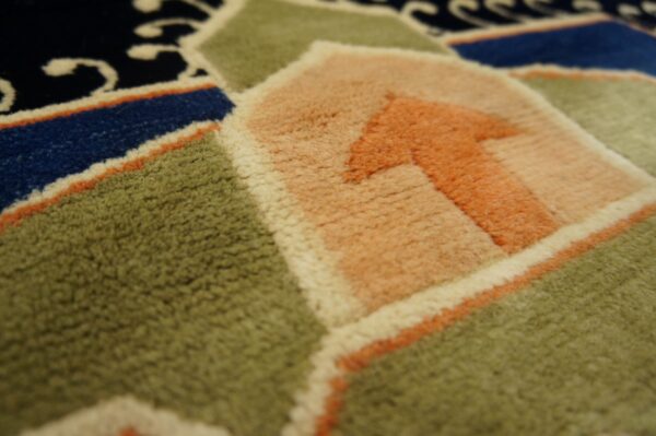 Close-up showing the rug's plush texture and geometric pattern in green, salmon, blue, and cream.