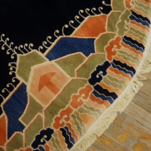 A plush, deep blue rug with colorful geometric and wave patterns rests on worn light wood flooring.