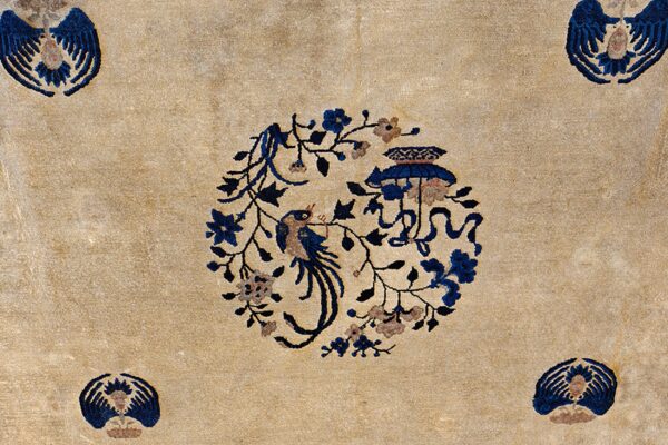 A textured beige rug features a central blue bird and flower medallion with smaller blue corner accents.