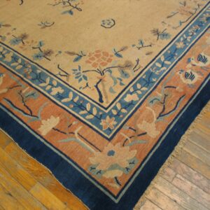 Close-up of a beige rug with indigo, sky blue, and coral floral borders on hardwood floor.