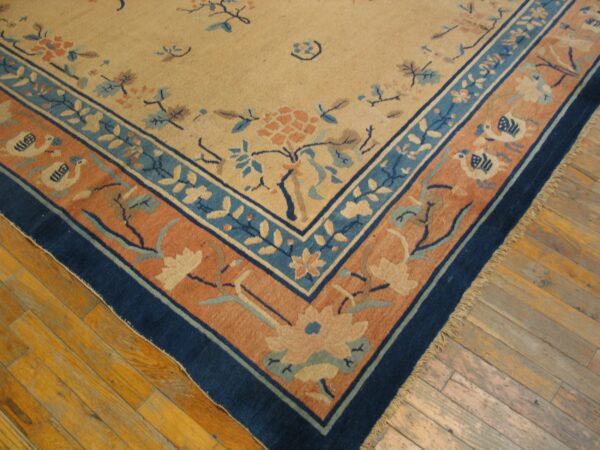 Close-up of a beige rug with indigo, sky blue, and coral floral borders on hardwood floor.
