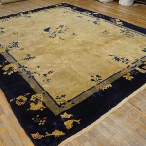 Golden field rug featuring scattered blue motifs and a wide navy border with stylized gold flowers, set on wood planks.