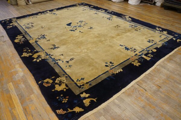 Golden field rug featuring scattered blue motifs and a wide navy border with stylized gold flowers, set on wood planks.