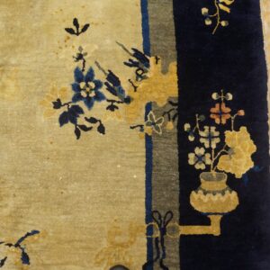 Light tan and navy blue rug with stylized florals and a vase motif sits on distressed wood planks.